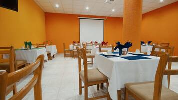 A conference room with white tables and chairs, a projector screen, and a large orange pillar.