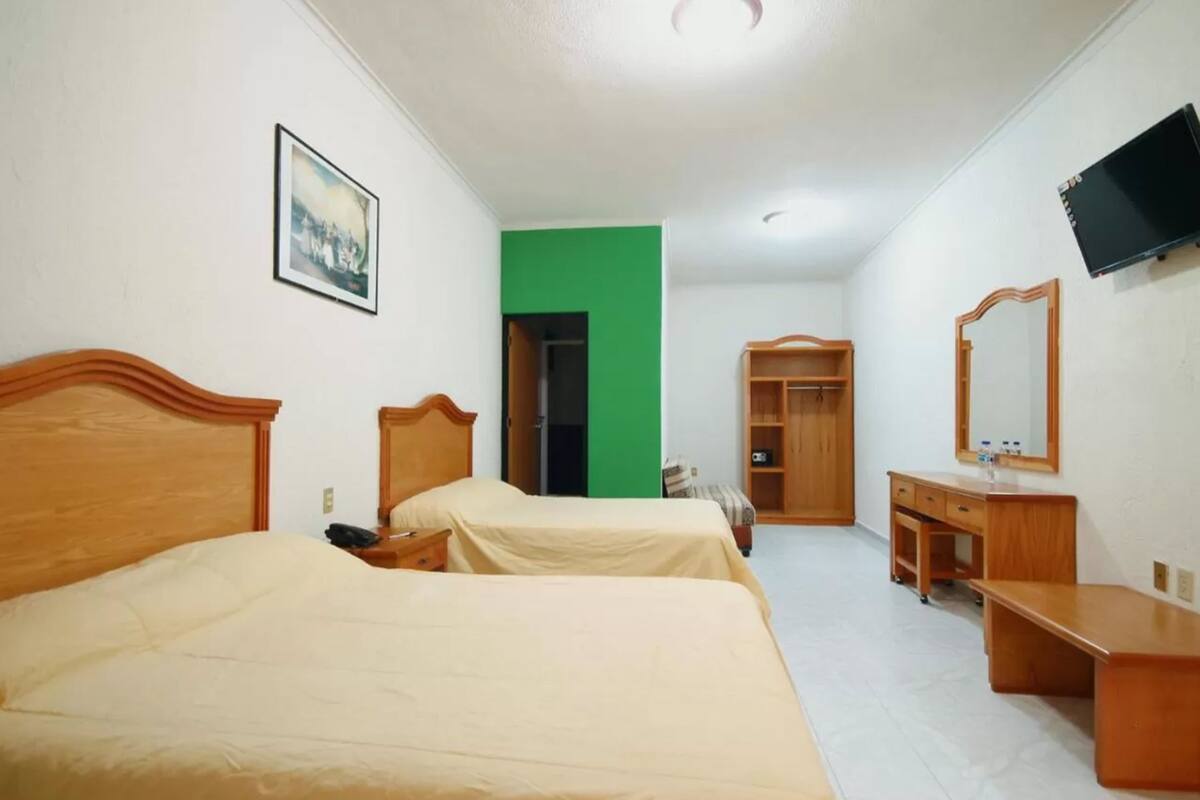 A hotel room with two beds, a green wall, a TV, a mirror, and a wooden dresser.