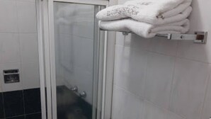 A bathroom with a glass shower enclosure, a toilet, and a towel rack with folded towels. - Hotel El Conquistador Monarca (Zitácuaro)