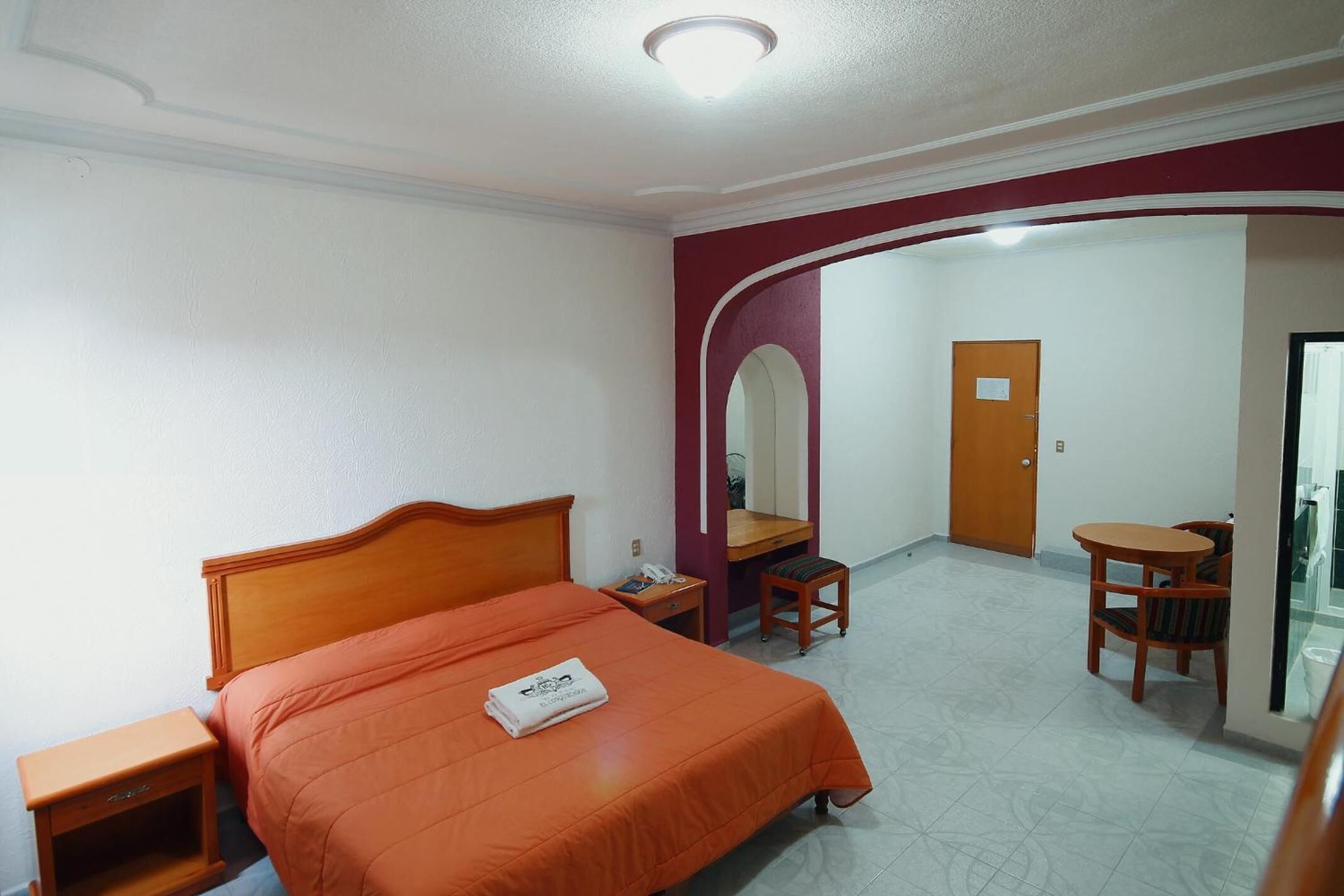Habitación de hotel con cama, escritorio, silla, espejo y puerta.