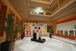 A hotel lobby with a high ceiling, a central seating area, and a wall decorated with framed artwork. - Hotel El Conquistador Monarca (Zitácuaro)