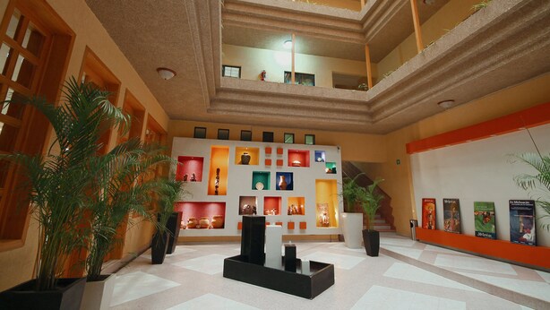 A multi-level atrium with a central staircase, potted plants, and a display of framed pictures on the walls. - Hotel El Conquistador Monarca (Zitácuaro)