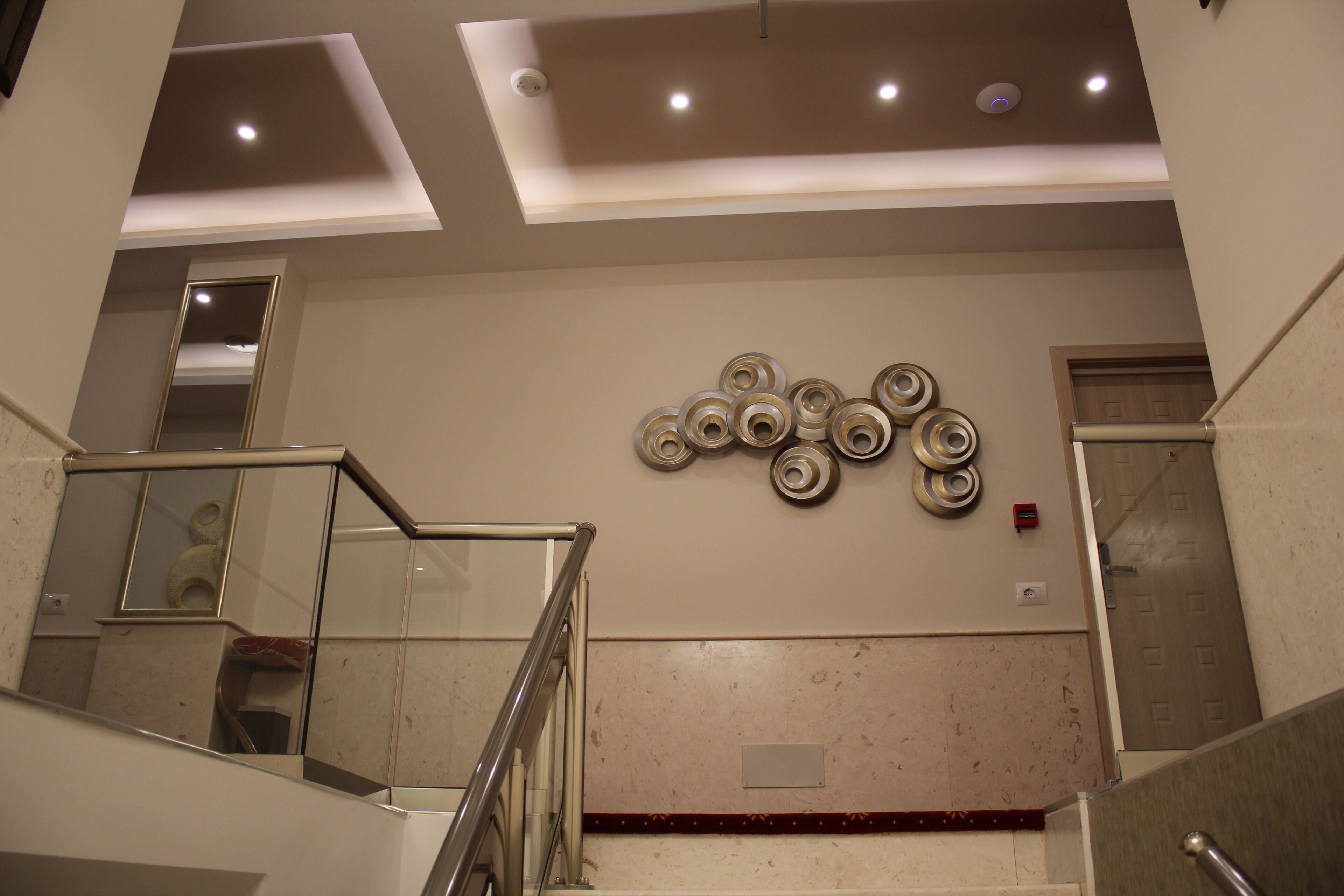 Een modern interieur met een glazen balustrade, een decoratieve wand met cirkelvormige patronen en een ingedimde verlichte plafond.