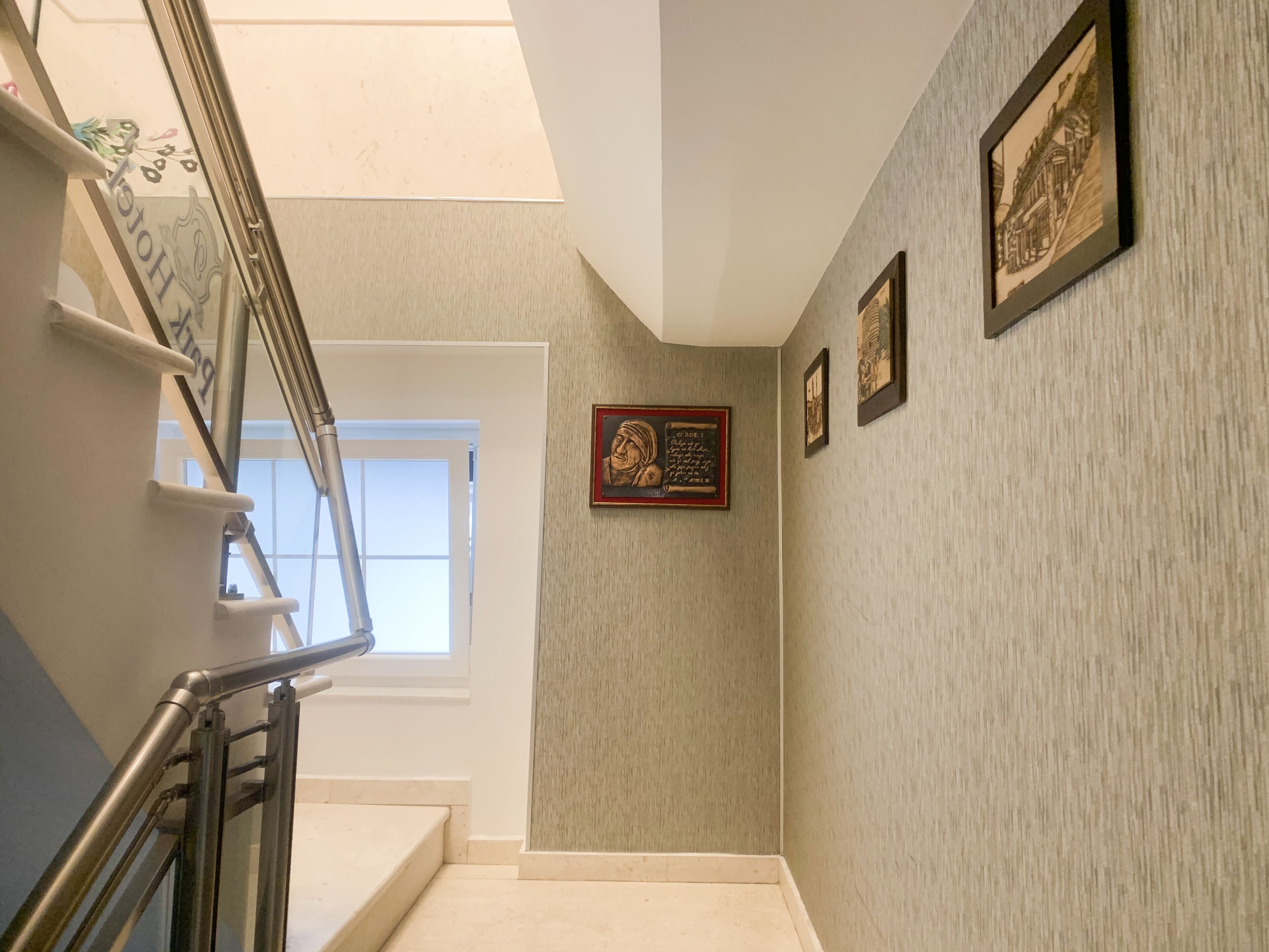 A staircase with a metal handrail, a window at the top, and a wall with framed pictures.