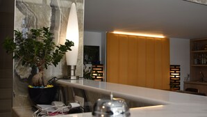 Un baño moderno con pared de mármol, una planta en maceta, un espejo y una zona de tocador con iluminación amarilla.