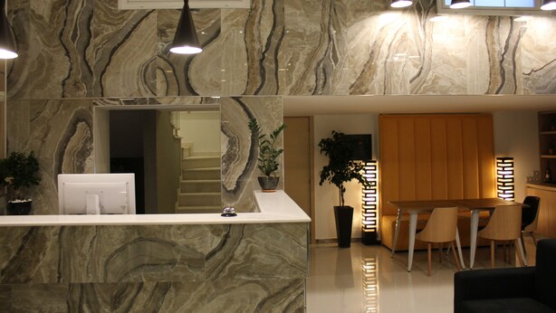 Un interior moderno con encimera de mármol, mostrador de recepción, escalera, zona de comedor con sillas e iluminación colgante.