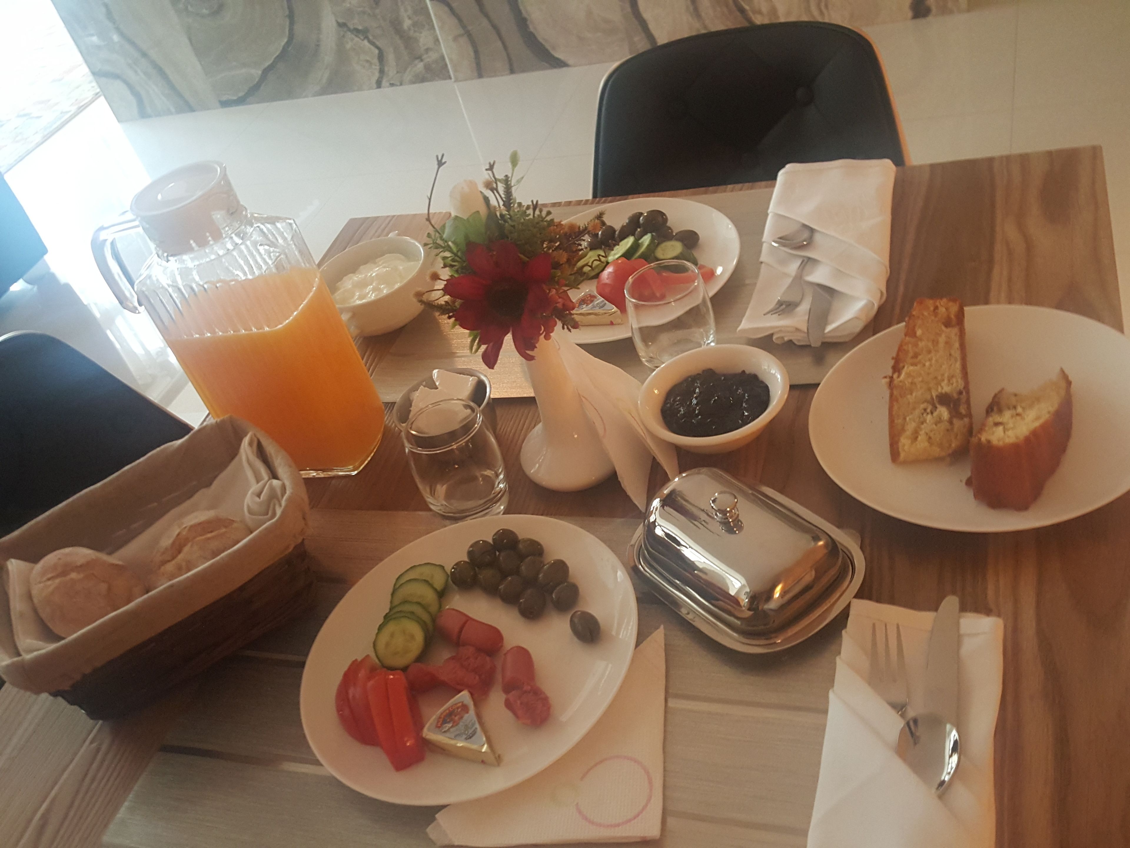 Une table de petit-déjeuner avec une variété d’aliments, notamment du pain, des fruits et une carafe de jus d’orange.