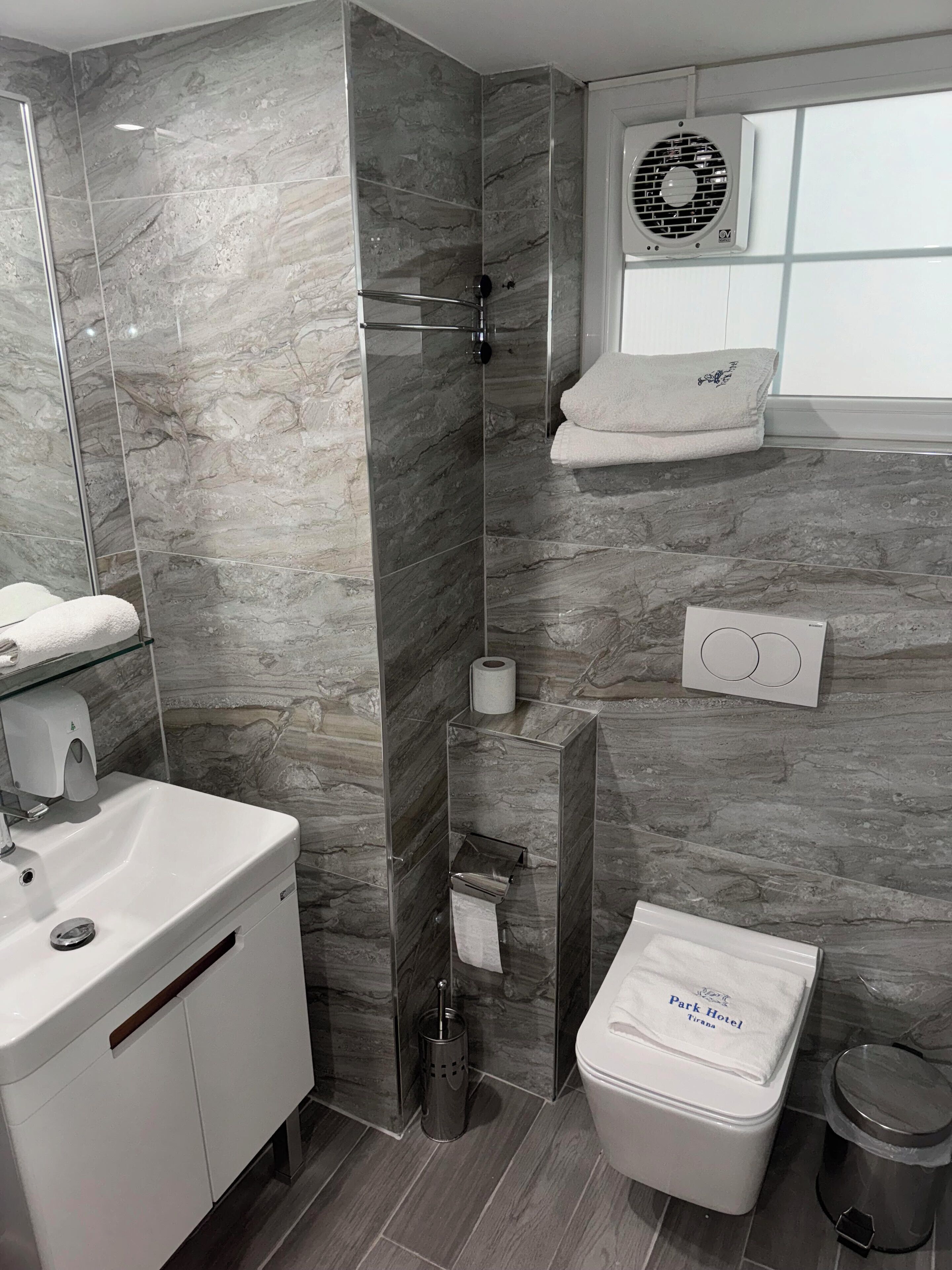 Ein modernes Badezimmer mit Duschkabine aus Glas, einem weißen Waschbecken, einer Toilette und einem Handtuchhalter.