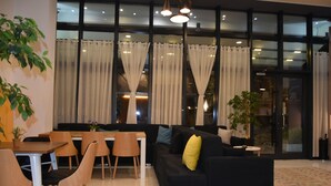 Una sala de estar moderna con un sofá negro, sillas de madera, una mesa de comedor y ventanas amplias con cortinas.