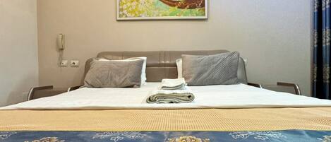 A hotel room with a bed, a painting on the wall, an air conditioning unit, and a telephone.