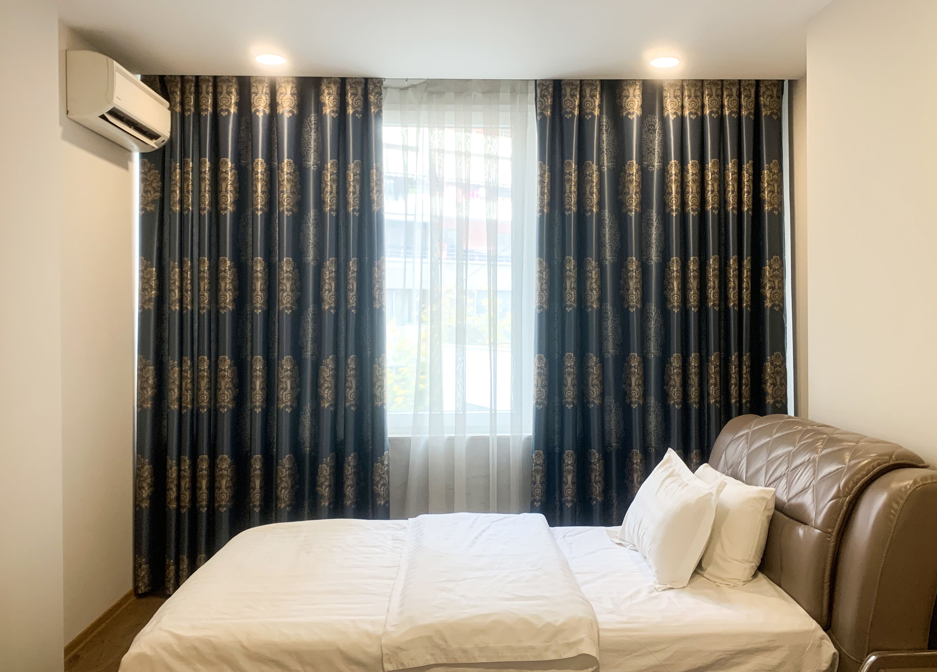 Une chambre d’hôtel comprenant un lit, une fenêtre avec des rideaux, un appareil de climatisation et un climatiseur fixé au mur.