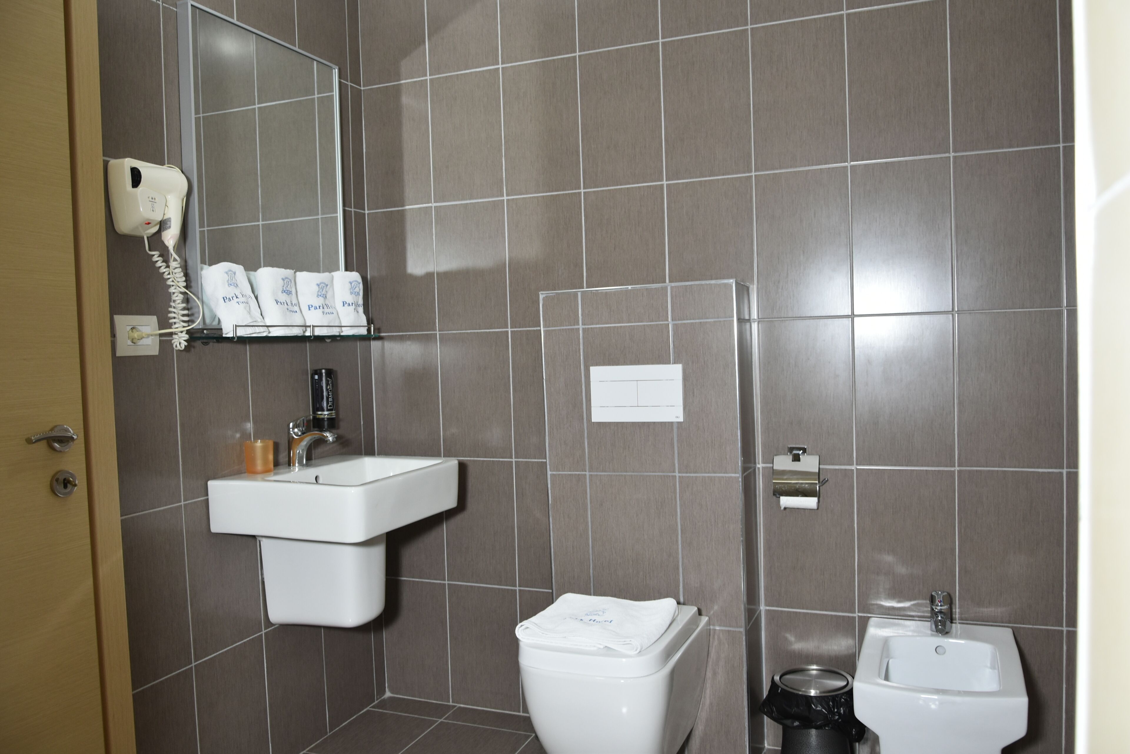 Casa de banho com lavatório, sanita e secador de cabelo fixado na parede.