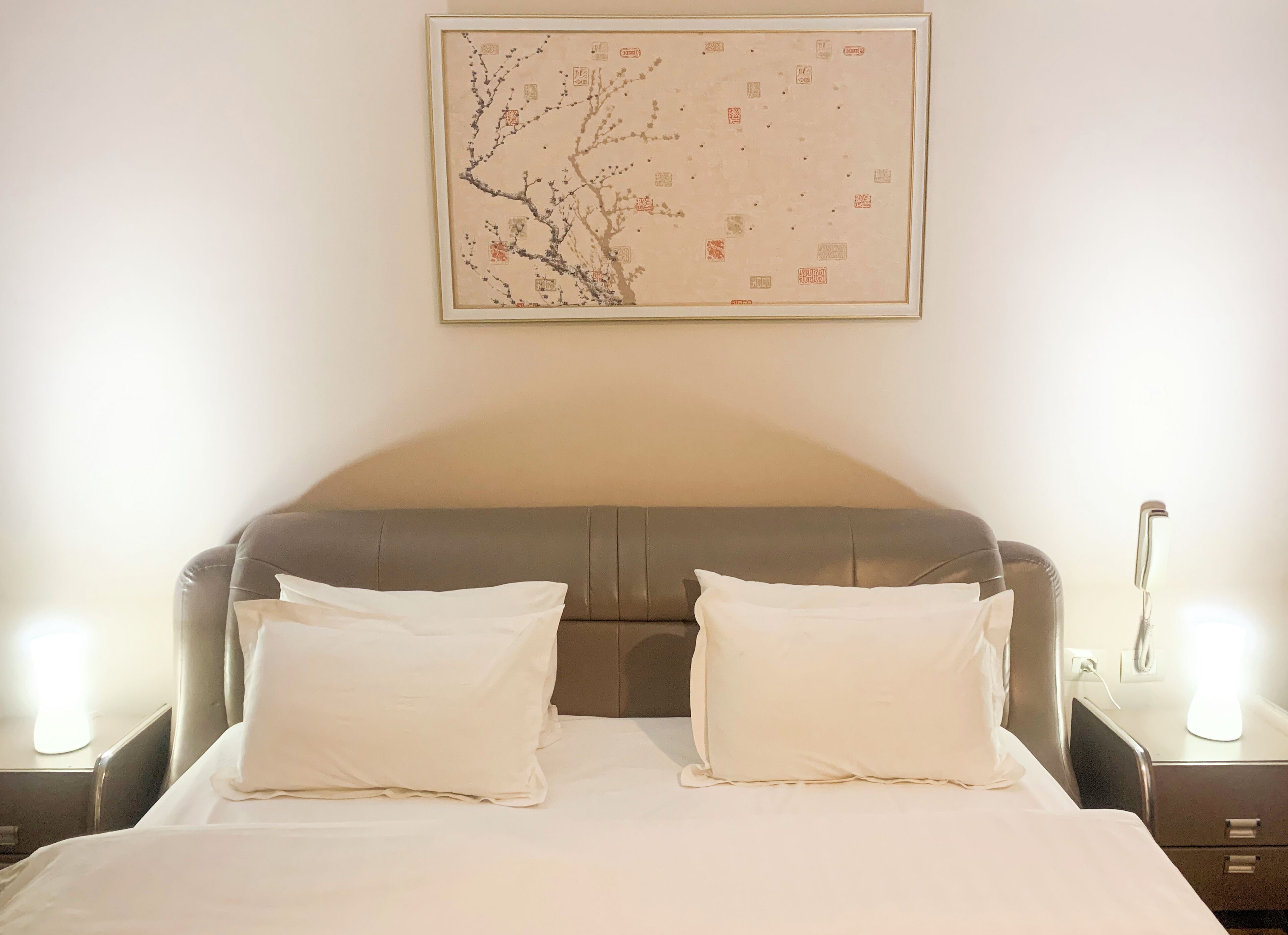 Una cama bien hecha con dos almohadas, un cabecero y una obra de arte enmarcada encima.