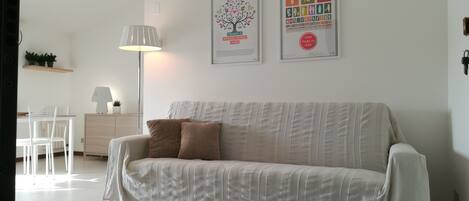 A modern living room with a sofa, a lamp, a desk with a computer, and two framed posters on the wall.