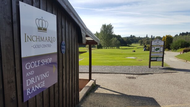 Segnaletica per un negozio di golf e un campo pratica, una bottiglia di whisky scozzese e un campo da golf sullo sfondo.