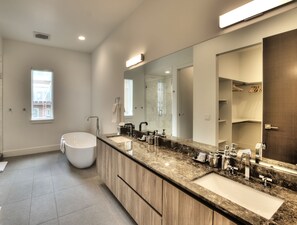 Une salle de bain moderne dotée d’un grand meuble-lavabo, de deux vasques, d’une baignoire et d’un grand miroir.