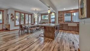 Una cocina amplia con una isla central, piso de madera, ventanas grandes y luminarias modernas.