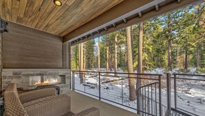 Un espacio de estar al aire libre cubierto, con mobiliario de mimbre, chimenea de piedra y vistas a un bosque nevado.