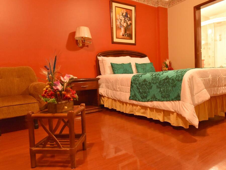 Una habitación de hotel con una cama de madera, una mesita de noche, una lámpara, una silla y un jarrón con flores.