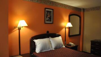 Una habitación de hotel con cama, dos lámparas de noche, una mesita de noche, un espejo y un aparador.