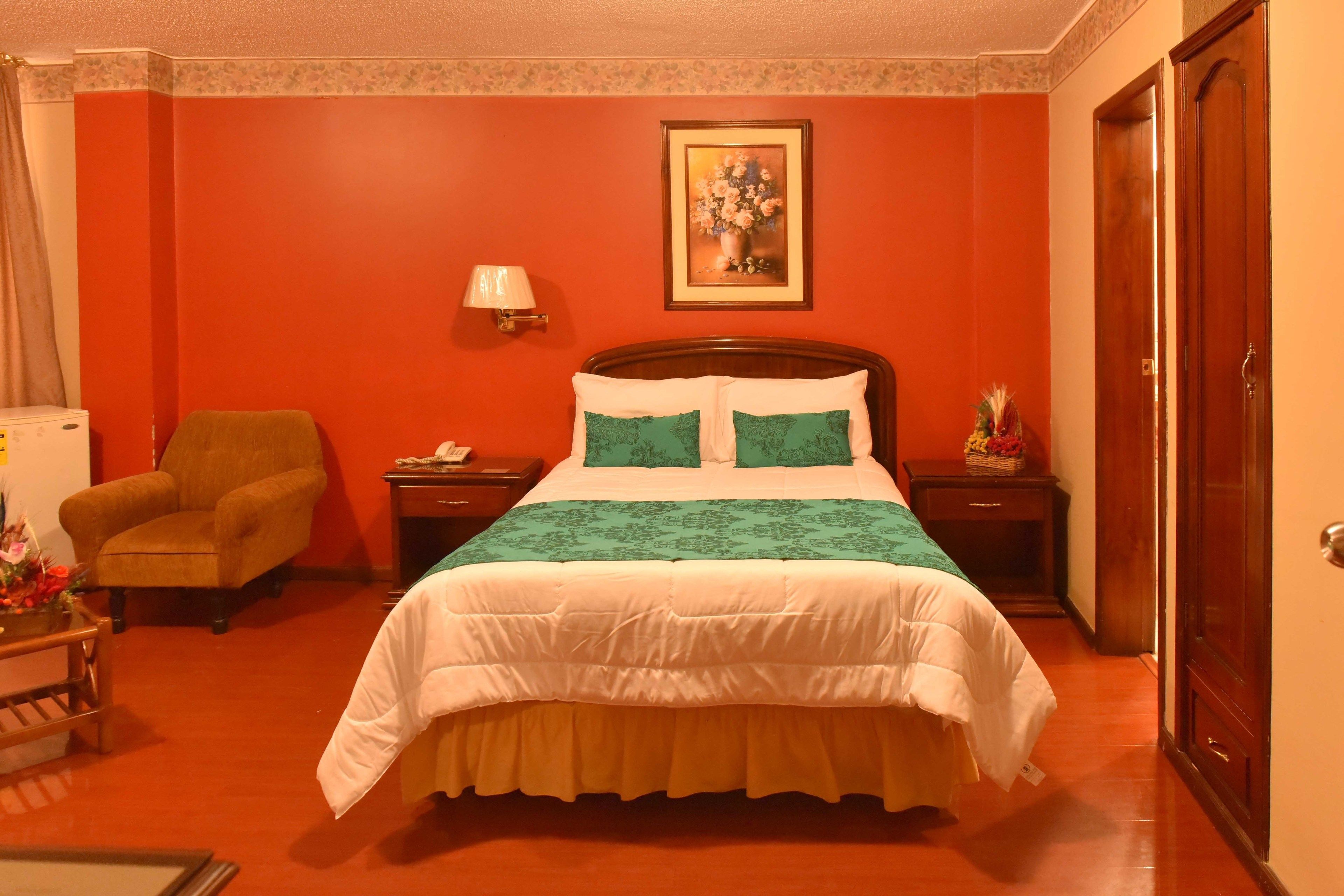 Una habitación de hotel con una cama grande, una silla, una mesita de noche y una lámpara.