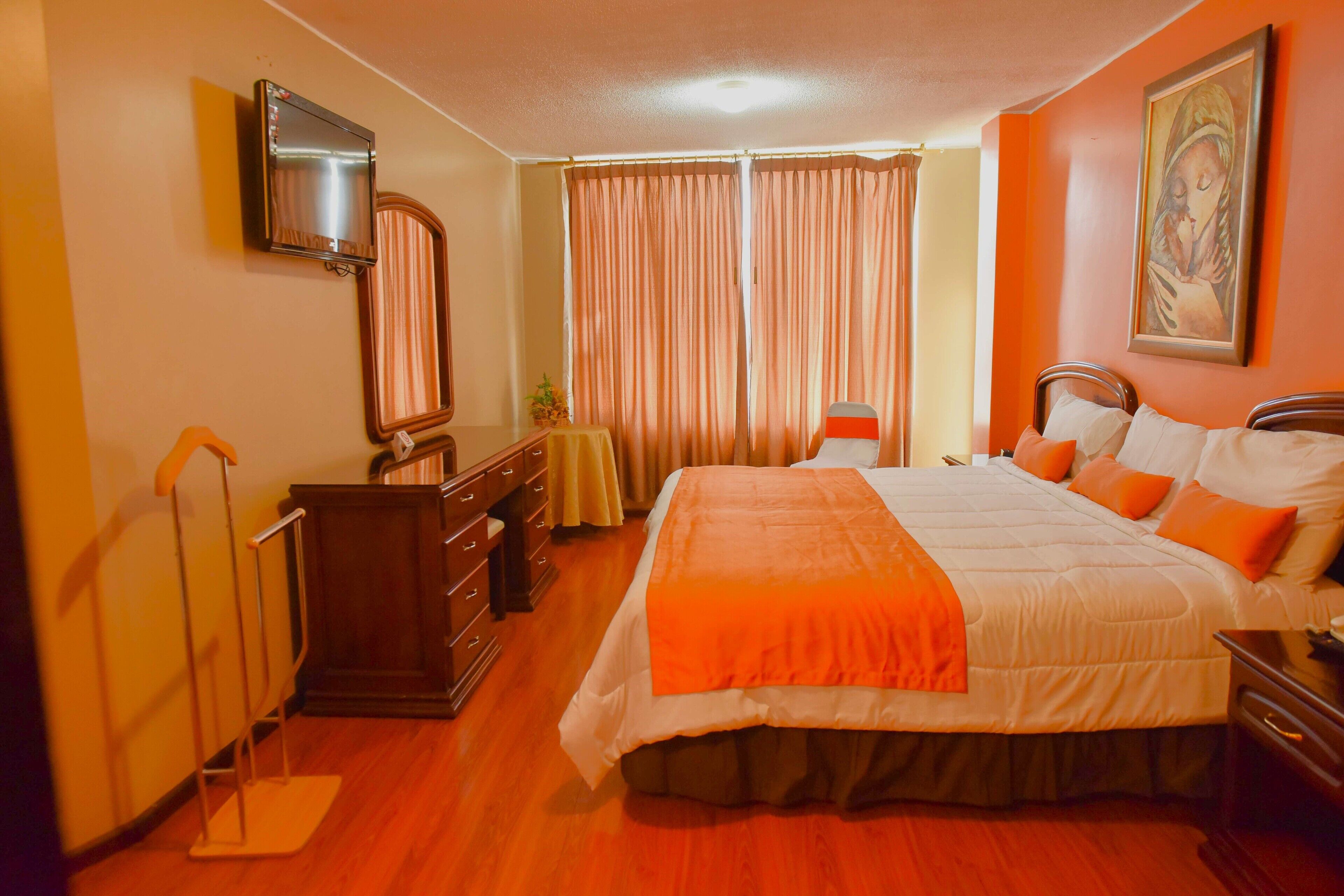 A hotel room with a large bed, a TV mounted on the wall, a dresser, and a painting on the wall.
