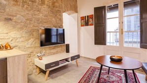 Una sala moderna con pared de piedra, televisor de pantalla plana, mueble blanco para entretenimiento, una mesa de centro redonda y un tapete rojo con estampado.