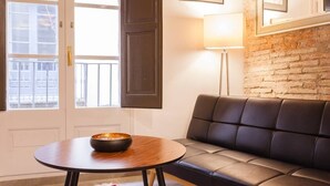 Una sala de estar moderna con un sofá de cuero, una mesa redonda de madera con un cuenco, una lámpara de pie y una pared de ladrillo.