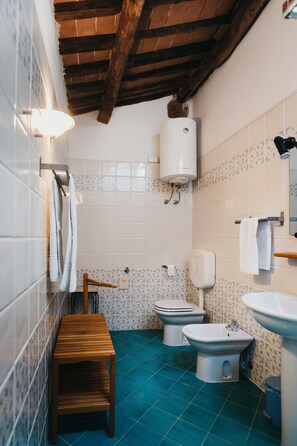 Une salle de bain avec un banc en bois, des toilettes, un bidet et un lavabo.
