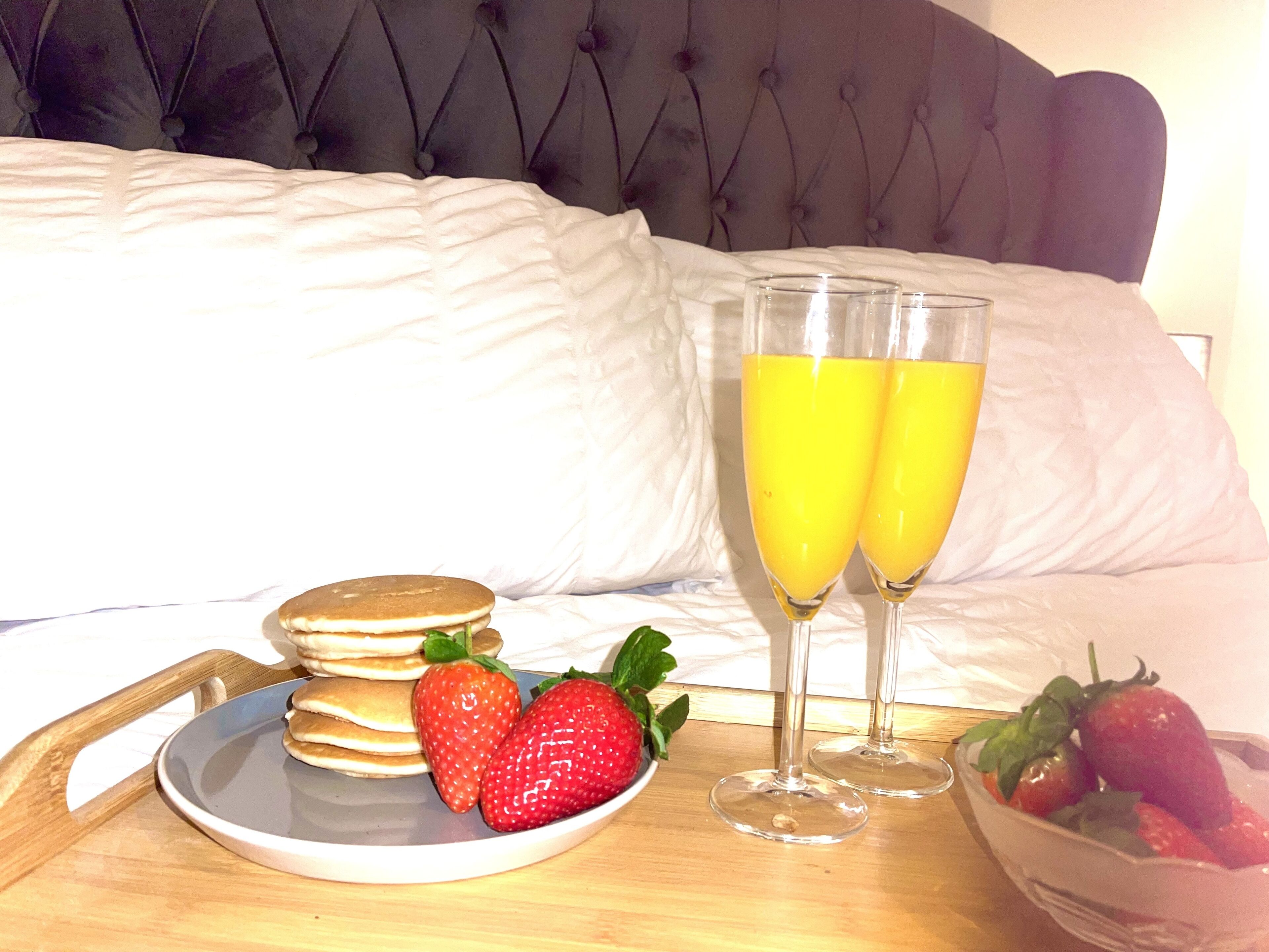Preparación para el desayuno con tortitas, fresas y dos vasos de zumo de naranja sobre una bandeja.