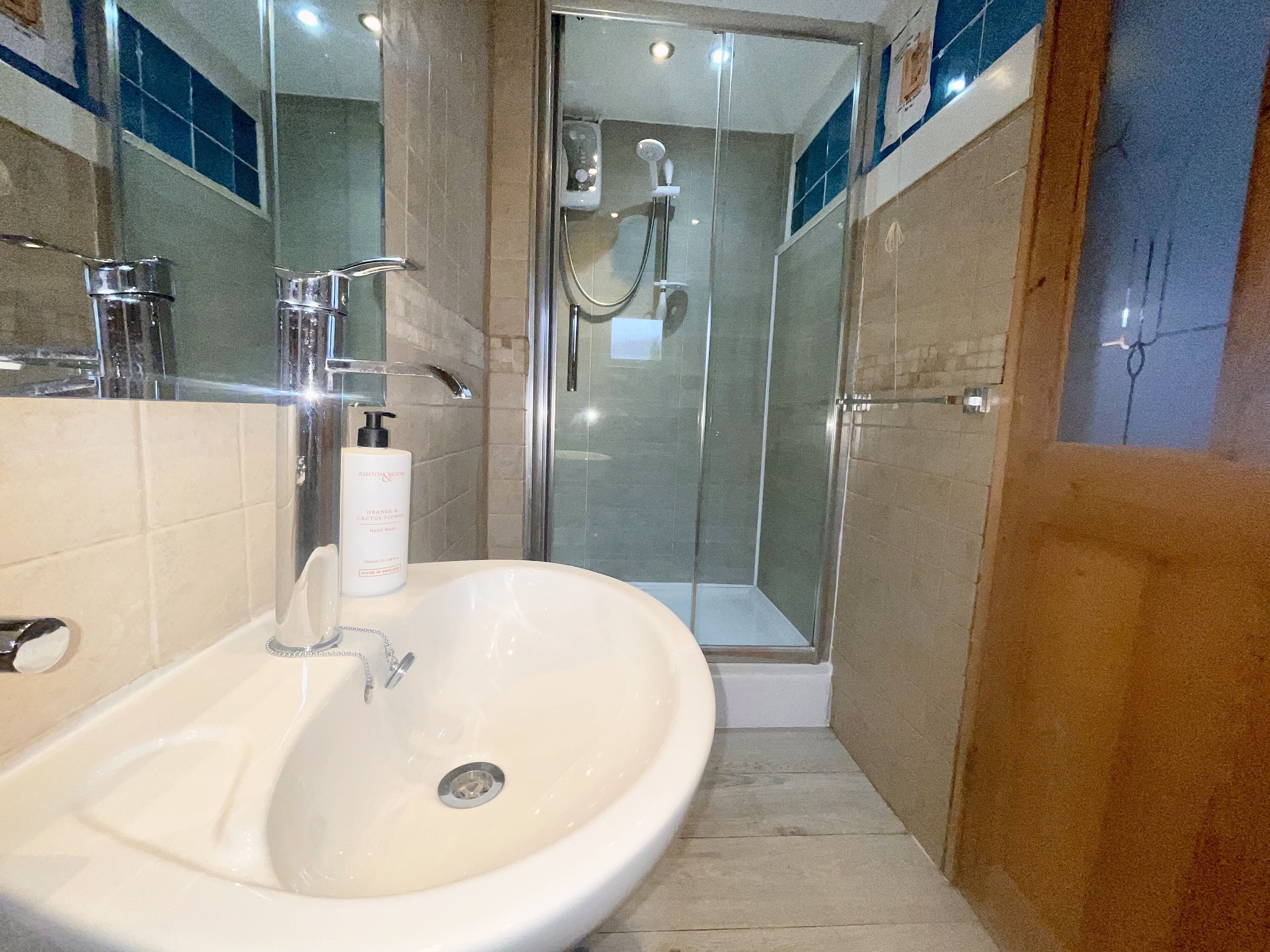 Un baño con lavamanos blanco, cabina de ducha con mampara de vidrio y espejo sobre el lavamanos.