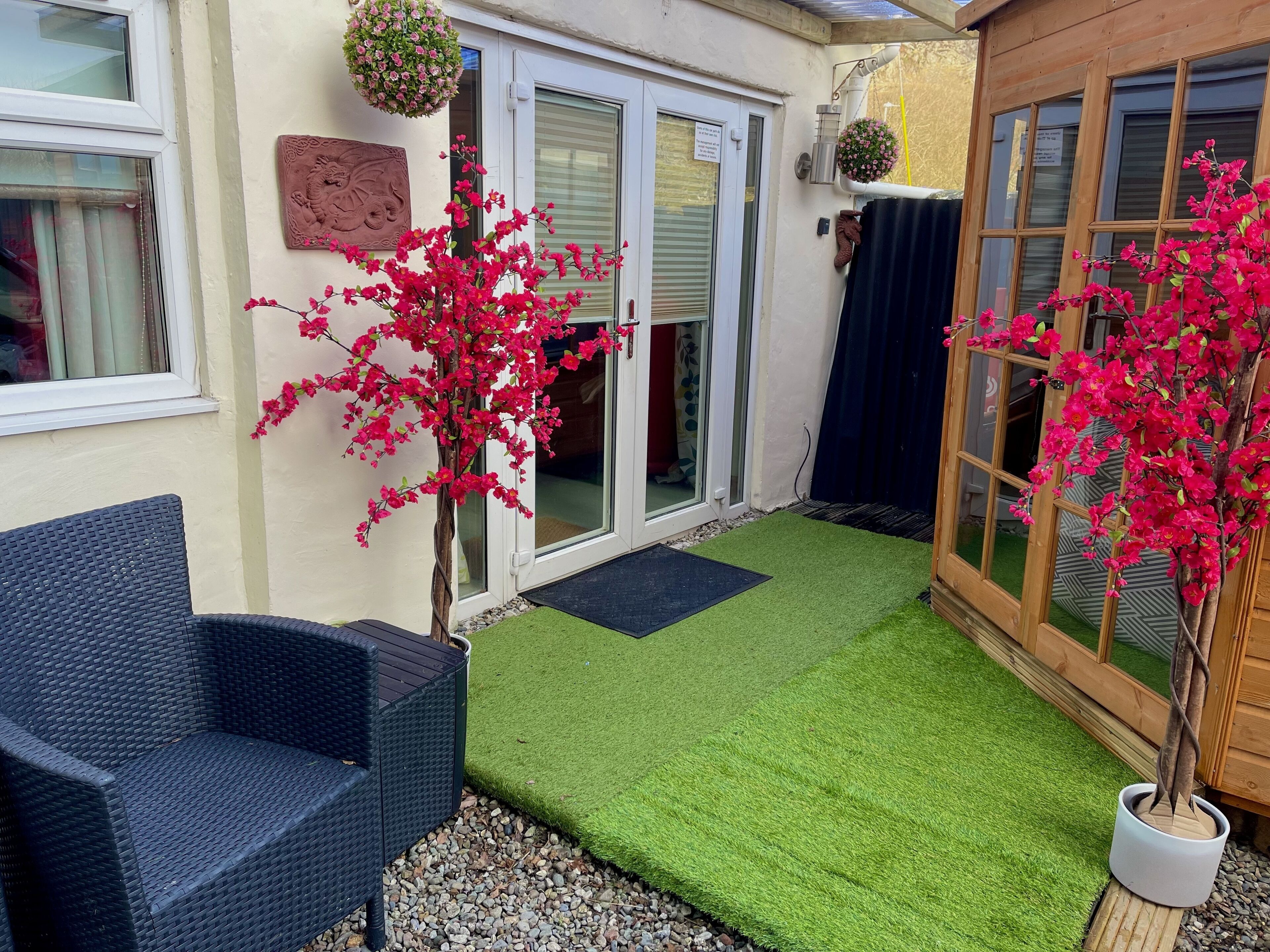 Un espacio al aire libre con césped artificial, una silla de mimbre y dos plantas en macetas.