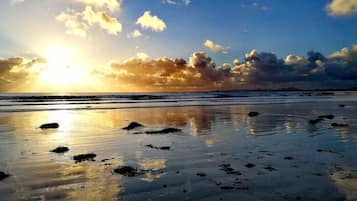Una spiaggia con sabbia bagnata e rocce sparse, un cielo sereno con nuvole e un orizzonte visibile.