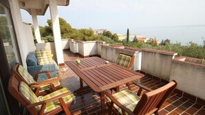 Un patio al aire libre con mesa y sillas de madera, un sofá y vistas al mar y las colinas.
