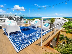 Eine Terrasse mit weißen Stühlen, einem blauen Teppich mit Muster und Lichterketten.