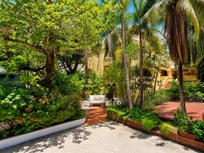 A courtyard with a white sofa, lush greenery, and a palm tree. - RentaElite Lovely 3 BR old city Cartagena w private pool (Cartagena)