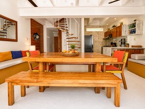Un espace repas moderne avec une table et des bancs en bois, une cuisine en arrière-plan et un escalier menant à un autre niveau.