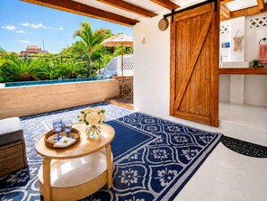 A poolside area with a wooden table, a blue patterned rug, and a view of a pool and greenery.