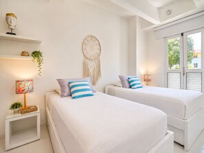 A hotel room with two beds, a wall-mounted dreamcatcher, and a window with shutters. - RentaElite Lovely 3 BR old city Cartagena w private pool (Cartagena)