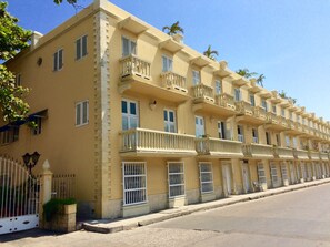 Um edifício com várias andares, varandas, entrada com portão e céu claro.