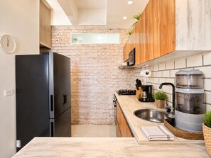 Een moderne keuken met een bakstenen muur, houten kastjes, een zwarte koelkast, een roestvrijstalen spoelbak en een koffiezetapparaat.
