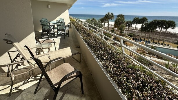 A balcony with a view of the beach, outdoor furniture, and a pool area.
