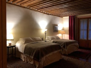 A room with two beds, wooden ceiling beams, a red curtain, and a patterned rug. - Seminario 12 (Mexico City)