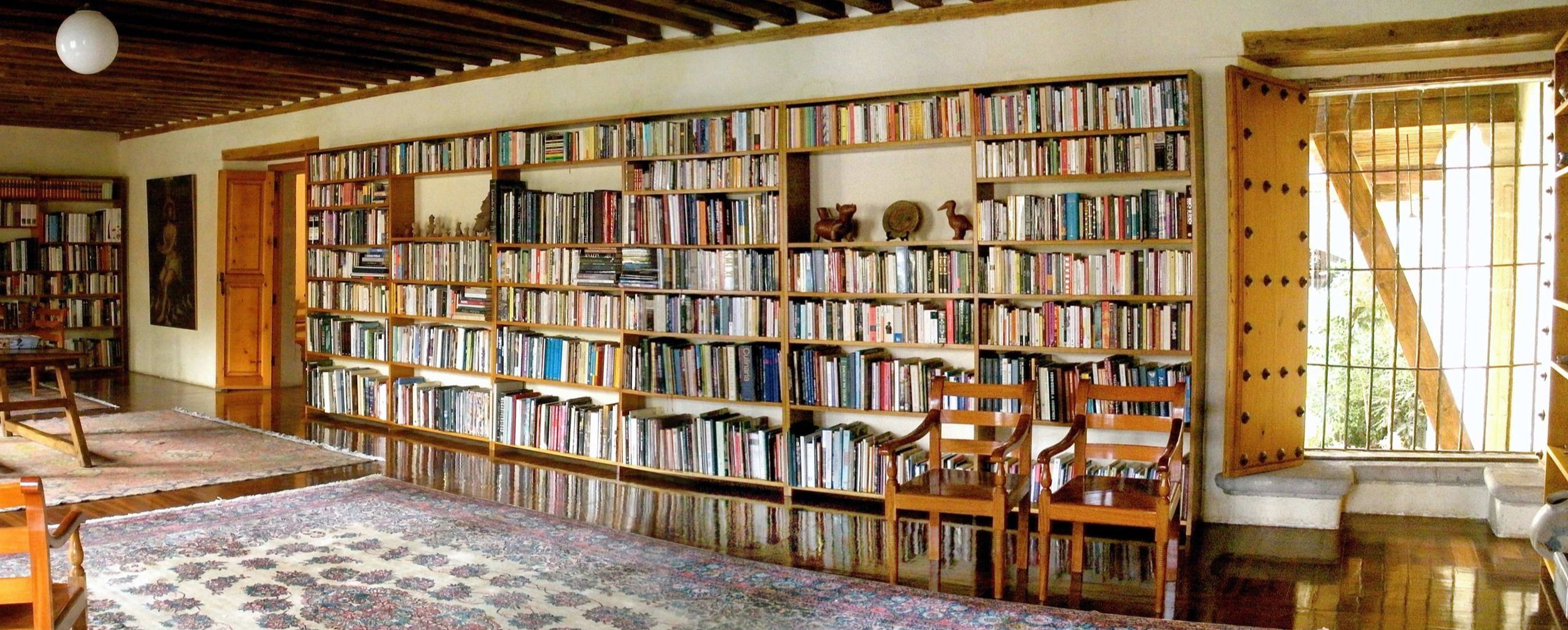 A library with wooden bookshelves filled with books, a patterned rug, and a wooden chair.