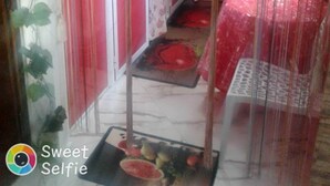 Une cuisine de taille réduite, équipée d’un évier, d’un petit plan de travail et d’un réfrigérateur. On y trouve une porte rouge et une fenêtre avec des rideaux.