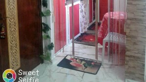 Une pièce avec une porte en bois, un séparateur rouge et blanc, un coin cuisine avec des placards rouges et un mur en pierre.