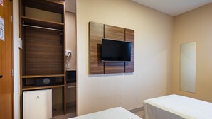 Een hotelkamer met een kledingkast, een aan de muur bevestigde televisie, een kleine koelkast en een bed.