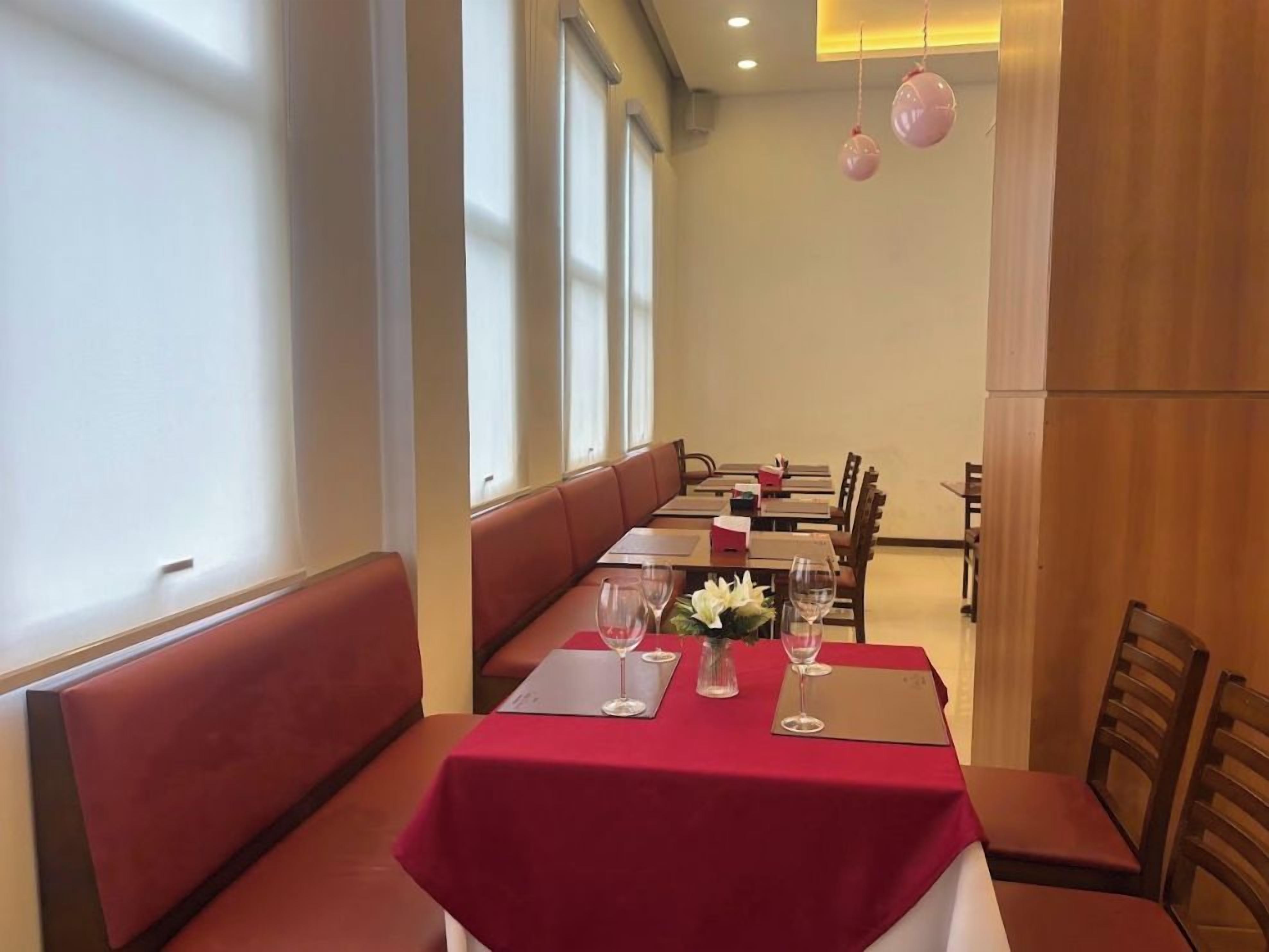 A restaurant with a red tablecloth, white flowers, and a row of booths.