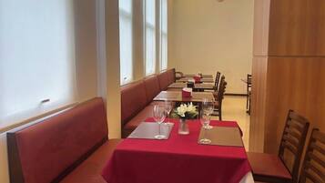 A restaurant with a red tablecloth, white flowers, and a row of booths.