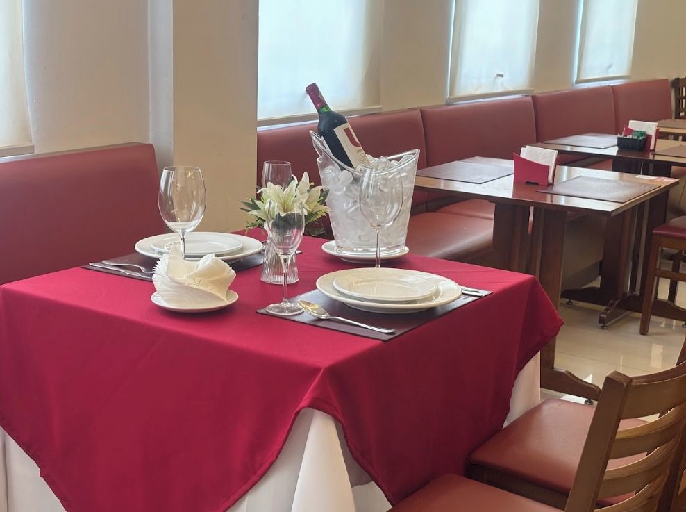 Ambiente de restaurante com uma mesa posta para dois, incluindo uma garrafa de champanhe, taças de vinho e um vaso com flores.